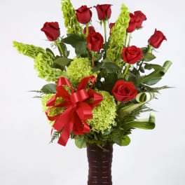 Red roses and green flowers in a tall vase with a red ribbon