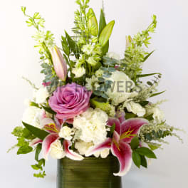 Pink rose and lily arrangement in a green glass vase