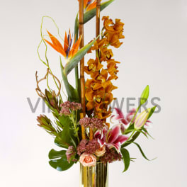 Tall tropical flower arrangement in a gold vase with orange and pink blooms
