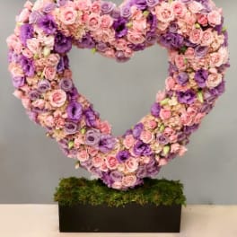 Large heart-shaped arrangement of pink and purple flowers on a moss-covered black rectangular base