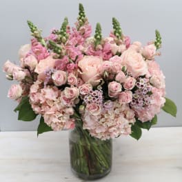 Large arrangement of soft pink roses, snapdragons, and hydrangeas in a clear glass vase