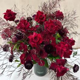 Deep red roses and burgundy blooms in a green vase