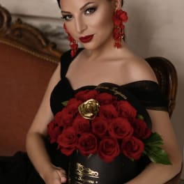 Woman in a black dress holding a black hatbox filled with red roses and one gold rose