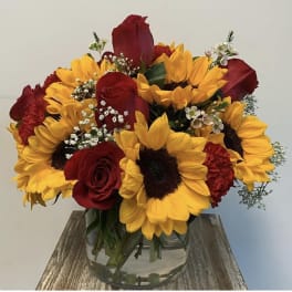 Bouquet of red roses and yellow sunflowers in a clear glass vase