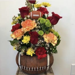 Football-shaped floral arrangement with red roses, carnations, and yellow daisies