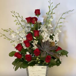 Red roses and white orchids in a tall silver planter with a succulent accent