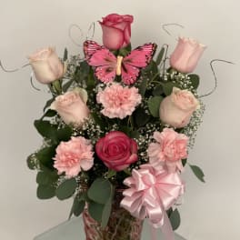 Pink roses and carnations in a glass vase with a butterfly decoration