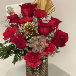 Red roses and carnations in a gold vase with decorative bows and a crown