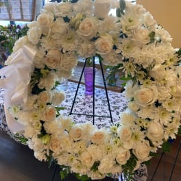 White floral wreath on a stand with roses and daisies