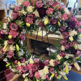 Large floral wreath with pink roses, lilies, and white blooms on a stand