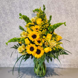 Tall bouquet of sunflowers and yellow roses in a glass vase