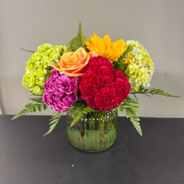 Colorful bouquet in a green glass vase with roses, carnations, and hydrangeas