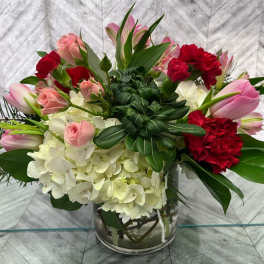 Mixed bouquet with pink tulips, red carnations, and white hydrangeas in a glass vase