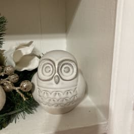 White ceramic owl figurine on a shelf beside holiday greenery