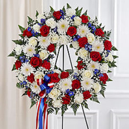 Red, white, and blue floral wreath on a stand with ribbon streamers