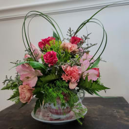 Pink floral arrangement in a teacup with heart-shaped loops