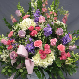 Large mixed floral arrangement in a white pedestal vase with pink ribbon