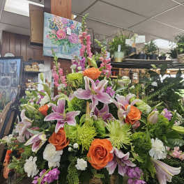 Large basket arrangement with pink lilies, orange roses, green mums, and white carnations on a small stand