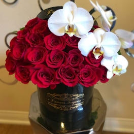 Red roses and white orchids arranged in a black hatbox