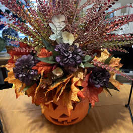 Halloween floral arrangement in a jack-o'-lantern container with autumn leaves