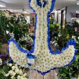 Large white floral anchor wreath with blue ribbon trim on a stand