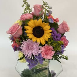 Mixed bouquet with a sunflower, pink roses, and purple flowers in a glass vase