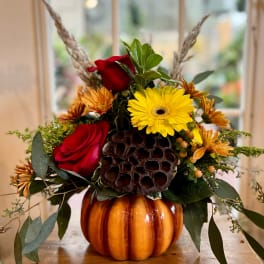 Autumn floral arrangement in a pumpkin container with red roses and yellow daisies