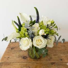 White roses and calla lilies in a glass vase with green and purple accents