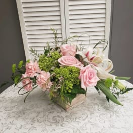 Low centerpiece of pink roses, pink carnations, green hydrangea and white lilies in a wooden cube vase