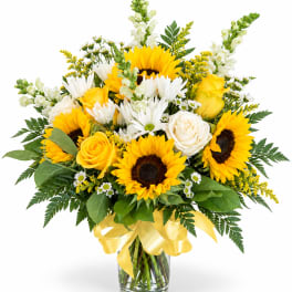 Bouquet of sunflowers, white daisies, and yellow roses in a glass vase