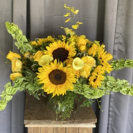 Yellow sunflower bouquet with roses and calla lilies in a glass vase