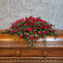 Red rose casket spray with trailing greenery on a wooden casket
