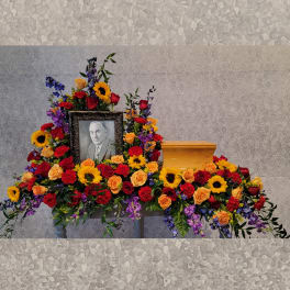 Colorful funeral casket spray with roses, sunflowers, and carnations around a framed portrait