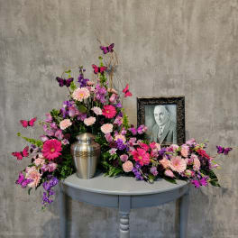 Pink and purple floral arrangement with a silver urn and framed portrait