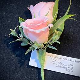 Pink rose boutonniere with green foliage and a white tag