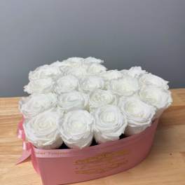 Heart-shaped pink box filled with tightly packed white roses on a wooden surface