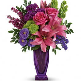 Pink lilies and roses in a purple vase with purple and green flowers