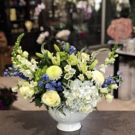 Mixed floral arrangement in a white pedestal vase with pale yellow, white, blue, and green blooms