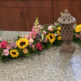 Floral funeral arrangement with sunflowers, pink roses, and snapdragons around a lantern