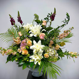 Tall floral arrangement with white lilies, peach roses, and purple spikes in a vase