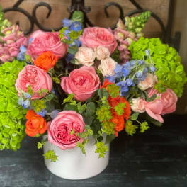 Pink and orange roses with blue flowers in a white vase