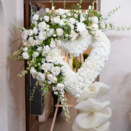 Heart-shaped white floral standing arrangement on an easel with a large white bow
