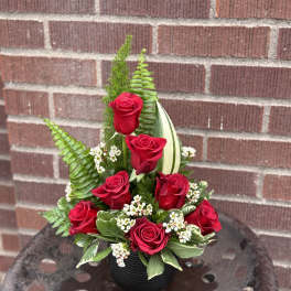 Red roses arranged in a black vase with greenery and white filler flowers