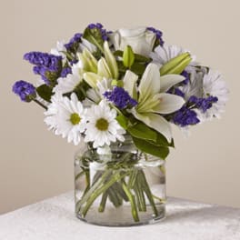 White lilies and daisies with purple filler in a glass vase