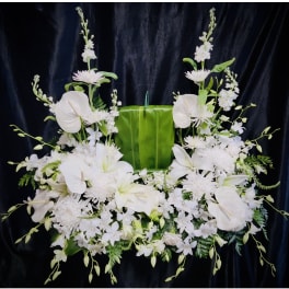 White floral funeral spray with lilies and orchids on a green backdrop