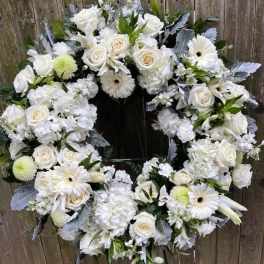 White floral wreath on a stand with roses and daisies