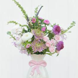 Pink and white mixed flower arrangement in a white vase with a pink bow