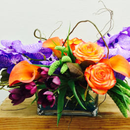 Orange roses and purple orchids in a glass vase