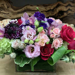 Mixed bouquet of roses, orchids, and hydrangeas in a low glass vase