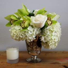 White roses and green orchids in a silver vase beside a candle